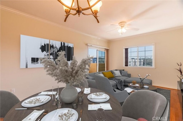 living room with ceiling fan with notable chandelier, ornamental molding, wood finished floors, and baseboards