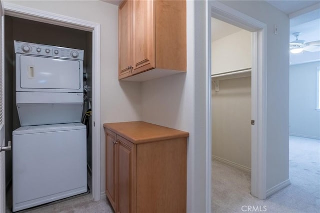 laundry room with light carpet, laundry area, baseboards, stacked washer and clothes dryer, and ceiling fan