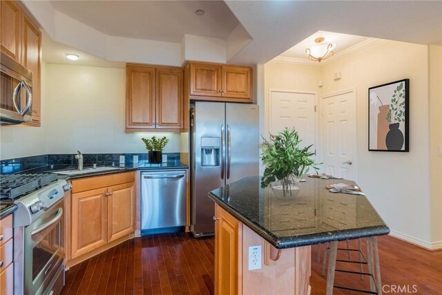 kitchen featuring dark stone countertops, dark wood-style flooring, stainless steel appliances, a kitchen bar, and a sink