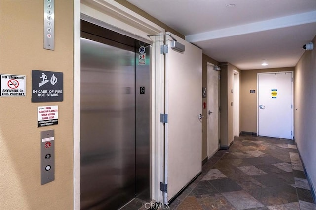 hall with baseboards, stone finish floor, and elevator