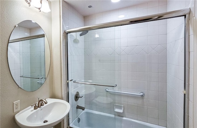 full bath with a textured wall, combined bath / shower with glass door, and a sink