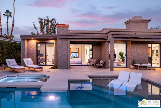 back house at dusk featuring a swimming pool with hot tub and a patio area