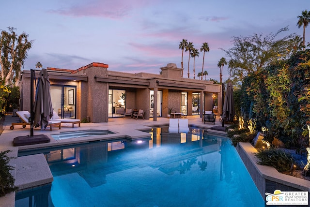 pool at dusk with an in ground hot tub and a patio