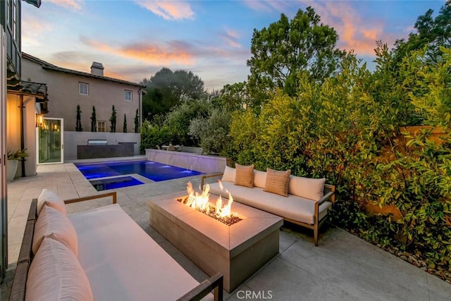 pool at dusk featuring a patio area, an in ground hot tub, and an outdoor living space with a fire pit