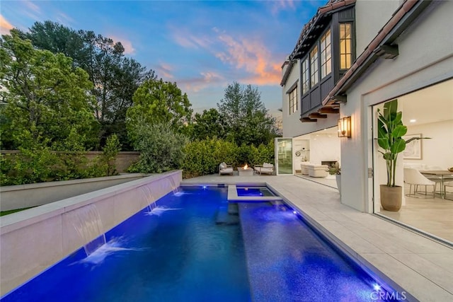 pool at dusk featuring pool water feature and a patio area