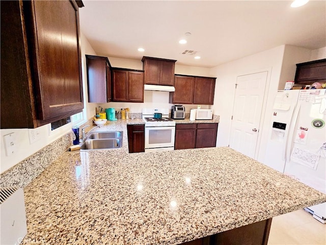 kitchen with kitchen peninsula, white appliances, light stone counters, dark brown cabinetry, and sink