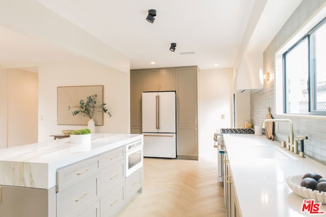 kitchen featuring tasteful backsplash, range hood, a kitchen island, light parquet floors, and high end white refrigerator