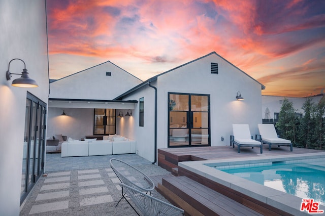 back house at dusk featuring outdoor lounge area and a patio