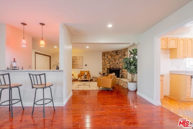 kitchen with pendant lighting, a stone fireplace, hardwood / wood-style floors, and a breakfast bar area