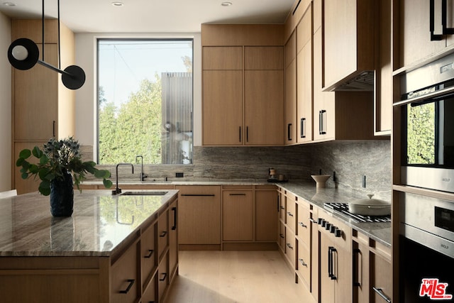 kitchen with dark stone countertops, gas cooktop, sink, hanging light fixtures, and stainless steel double oven