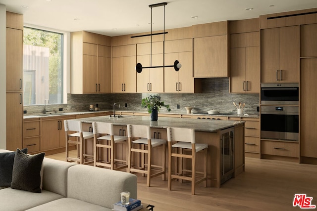 kitchen with a breakfast bar, pendant lighting, light brown cabinets, and a kitchen island with sink