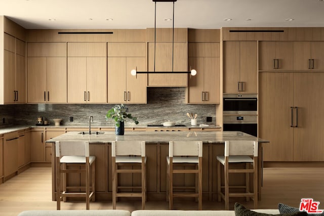 kitchen featuring light stone counters, light hardwood / wood-style floors, a center island with sink, and a breakfast bar