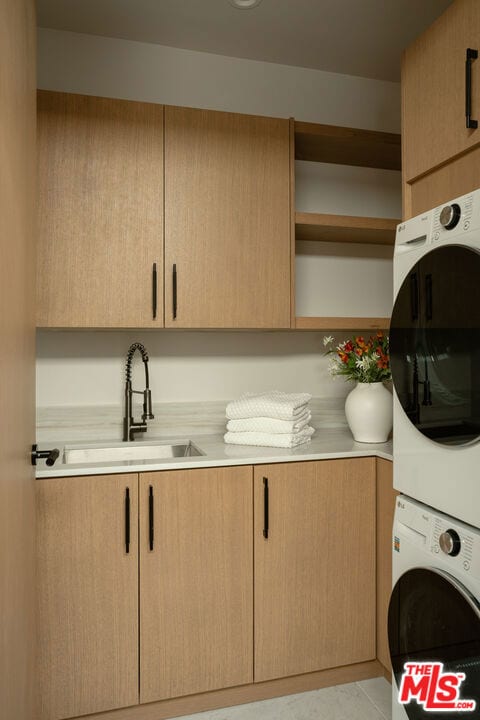 laundry room featuring cabinets, stacked washer / dryer, and sink