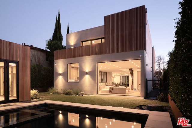 back house at dusk featuring a lawn, outdoor lounge area, a balcony, and a patio