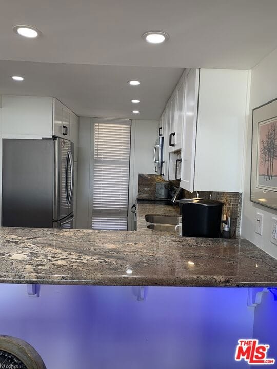 kitchen with dark stone countertops, white cabinets, a breakfast bar area, and appliances with stainless steel finishes