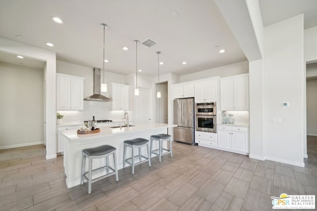 kitchen featuring white cabinetry, appliances with stainless steel finishes, a kitchen island with sink, wall chimney exhaust hood, and sink