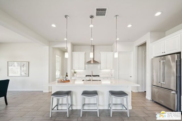 kitchen featuring an island with sink, wall chimney range hood, high end refrigerator, and white cabinetry