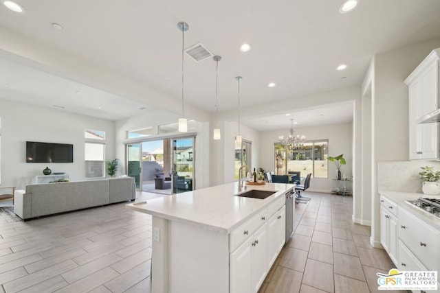 kitchen with decorative light fixtures, a notable chandelier, a center island with sink, sink, and white cabinetry