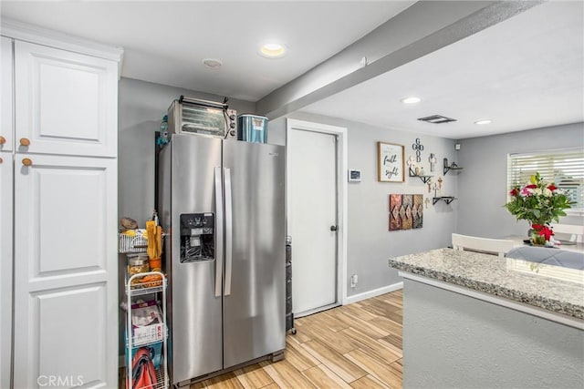 kitchen featuring stainless steel refrigerator with ice dispenser, light stone countertops, and white cabinets