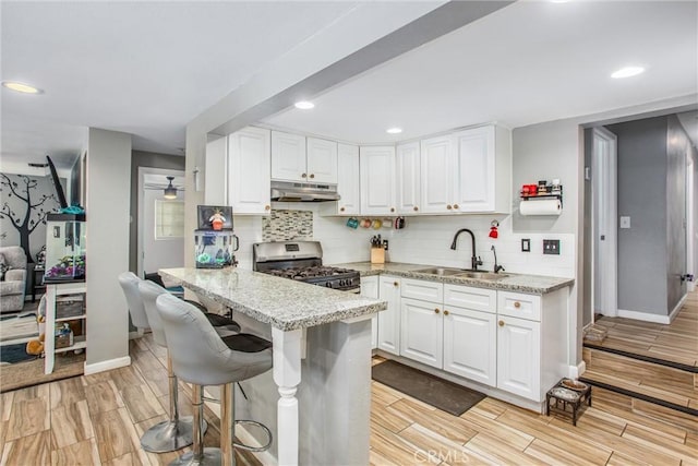 kitchen with white cabinetry, a kitchen breakfast bar, sink, stainless steel range with gas stovetop, and light stone counters