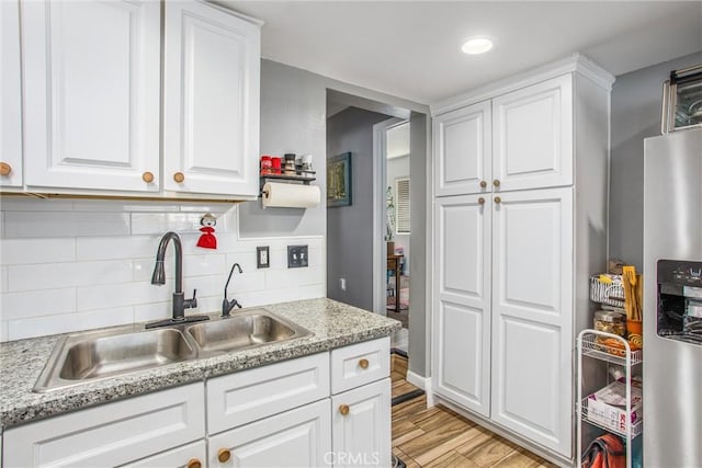 kitchen featuring light stone countertops, white cabinets, stainless steel refrigerator with ice dispenser, decorative backsplash, and sink