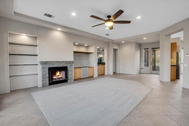 unfurnished living room with a stone fireplace, light tile patterned floors, built in features, and ceiling fan