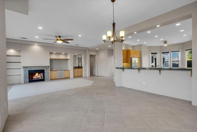 kitchen featuring pendant lighting, a stone fireplace, a breakfast bar, built in shelves, and kitchen peninsula