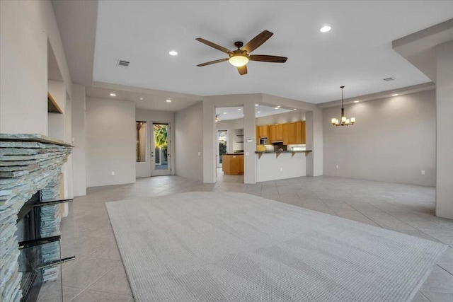 unfurnished living room featuring light tile patterned floors, a stone fireplace, and ceiling fan with notable chandelier