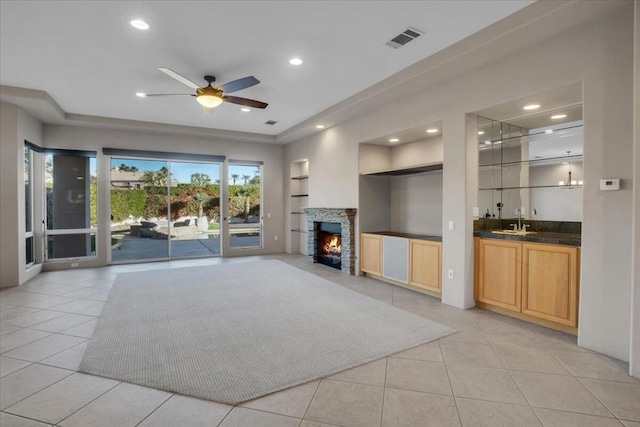 unfurnished living room featuring built in shelves, a stone fireplace, light tile patterned floors, wet bar, and ceiling fan