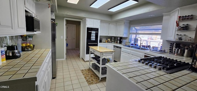 kitchen with tile counters, stainless steel appliances, white cabinets, and sink