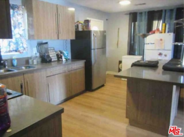 kitchen with stainless steel refrigerator, sink, light brown cabinets, and light wood-type flooring