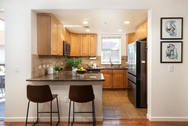 kitchen with stainless steel refrigerator, sink, dark stone countertops, a kitchen breakfast bar, and decorative backsplash