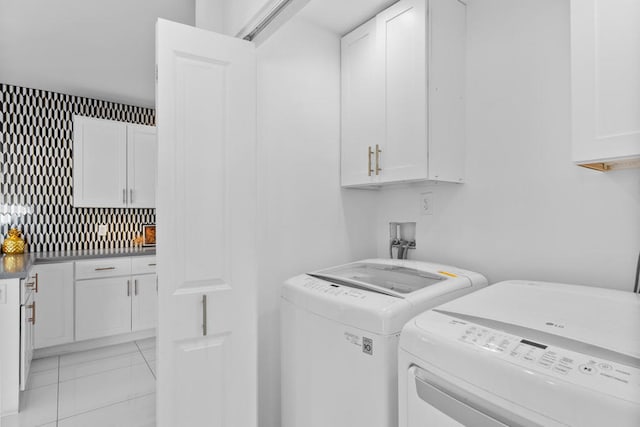 laundry room featuring washing machine and dryer, light tile patterned flooring, and cabinets