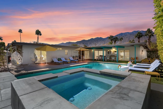 pool at dusk with a mountain view, a patio, and an in ground hot tub