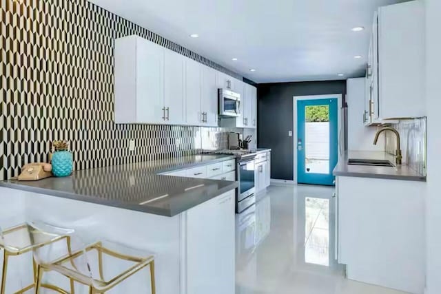 kitchen with white cabinetry, kitchen peninsula, stainless steel appliances, a kitchen breakfast bar, and sink