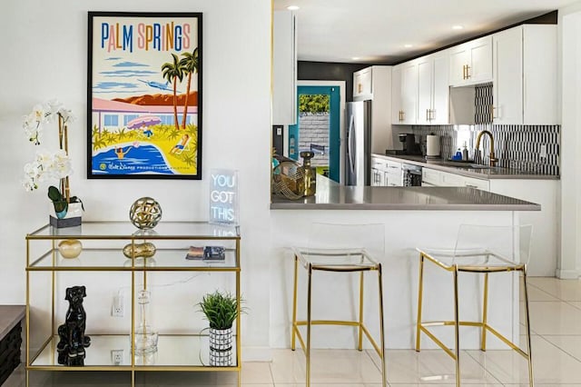 kitchen featuring white cabinetry, sink, stainless steel fridge, kitchen peninsula, and a breakfast bar area