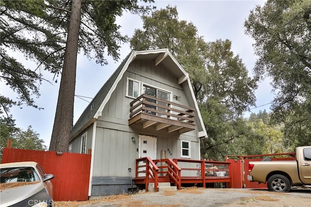 view of front of house featuring a gambrel roof, fence, and a balcony