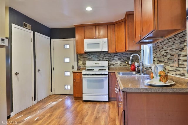 kitchen with tasteful backsplash, a sink, white appliances, brown cabinetry, and light wood-style flooring