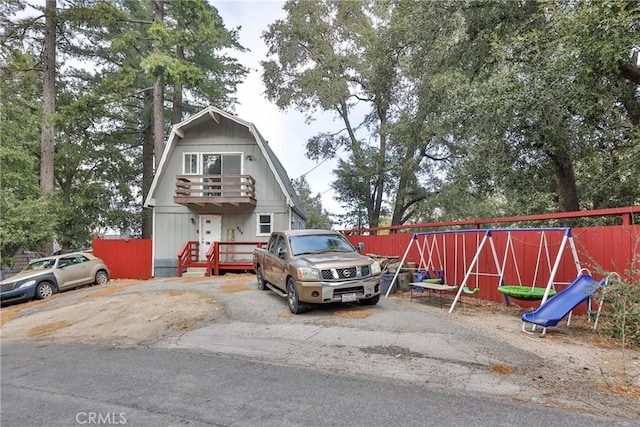 view of front facade featuring fence, a balcony, a gambrel roof, and a playground