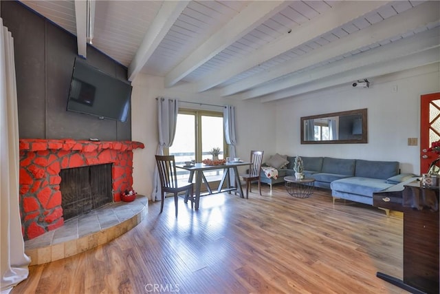 living area with light wood-style floors, beamed ceiling, and a fireplace with raised hearth