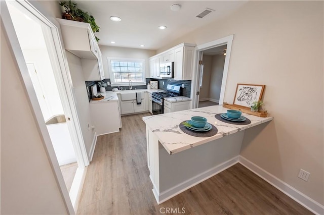 kitchen with white cabinetry, backsplash, stainless steel appliances, kitchen peninsula, and light wood-type flooring