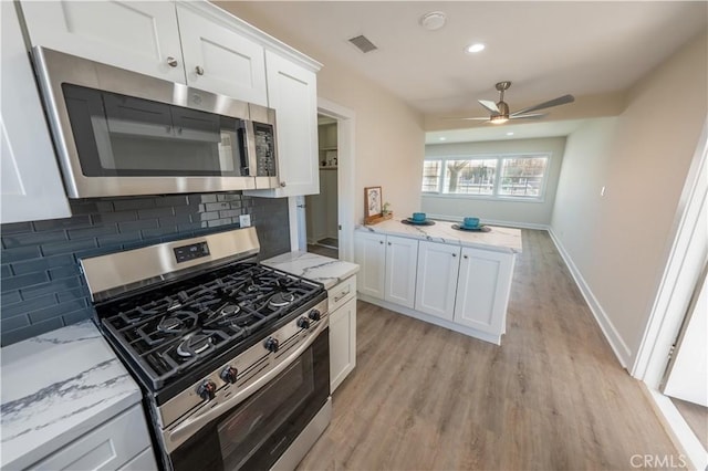 kitchen featuring white cabinetry, light stone counters, light hardwood / wood-style flooring, stainless steel appliances, and backsplash