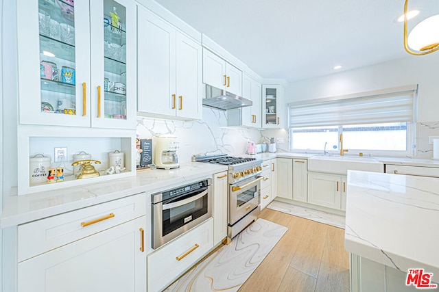 kitchen featuring tasteful backsplash, white cabinetry, light wood-type flooring, light stone countertops, and appliances with stainless steel finishes