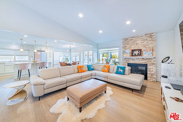 living room with a fireplace, high vaulted ceiling, a chandelier, light hardwood / wood-style flooring, and sink