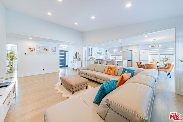 living room featuring vaulted ceiling, an inviting chandelier, and light hardwood / wood-style flooring