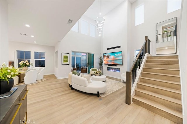 living room featuring a healthy amount of sunlight, a towering ceiling, and light hardwood / wood-style flooring