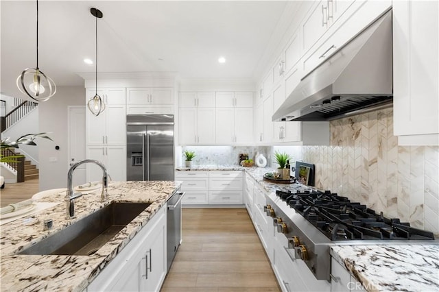 kitchen with stainless steel appliances, pendant lighting, white cabinets, light stone counters, and sink