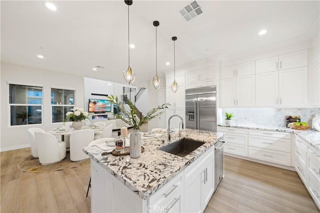 kitchen featuring white cabinetry, stainless steel appliances, tasteful backsplash, sink, and a center island with sink