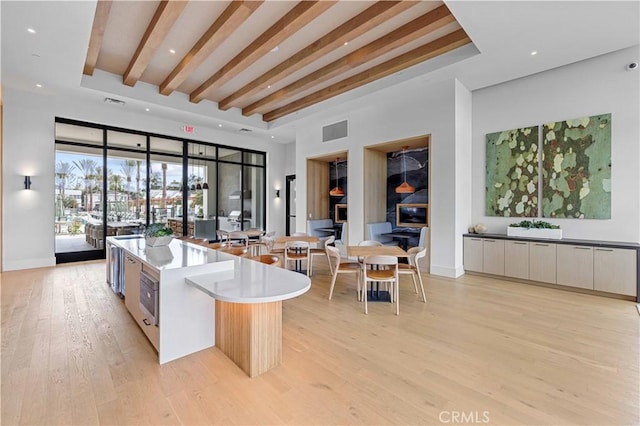 kitchen featuring stainless steel microwave, a kitchen island, a towering ceiling, white cabinetry, and light hardwood / wood-style flooring