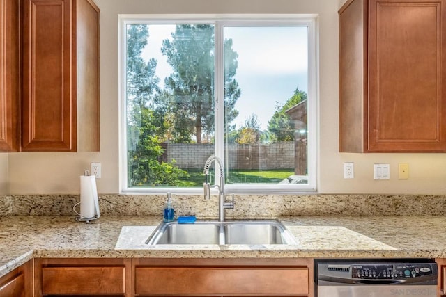 kitchen with light stone countertops, dishwasher, and sink